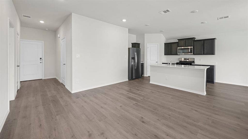 Kitchen with stainless steel appliances, open floor plan, an island with sink, recessed lighting, and dark wood finished floors