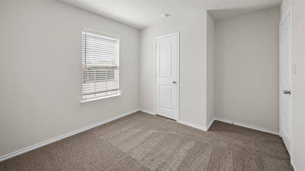 Unfurnished bedroom with dark colored carpet and baseboards