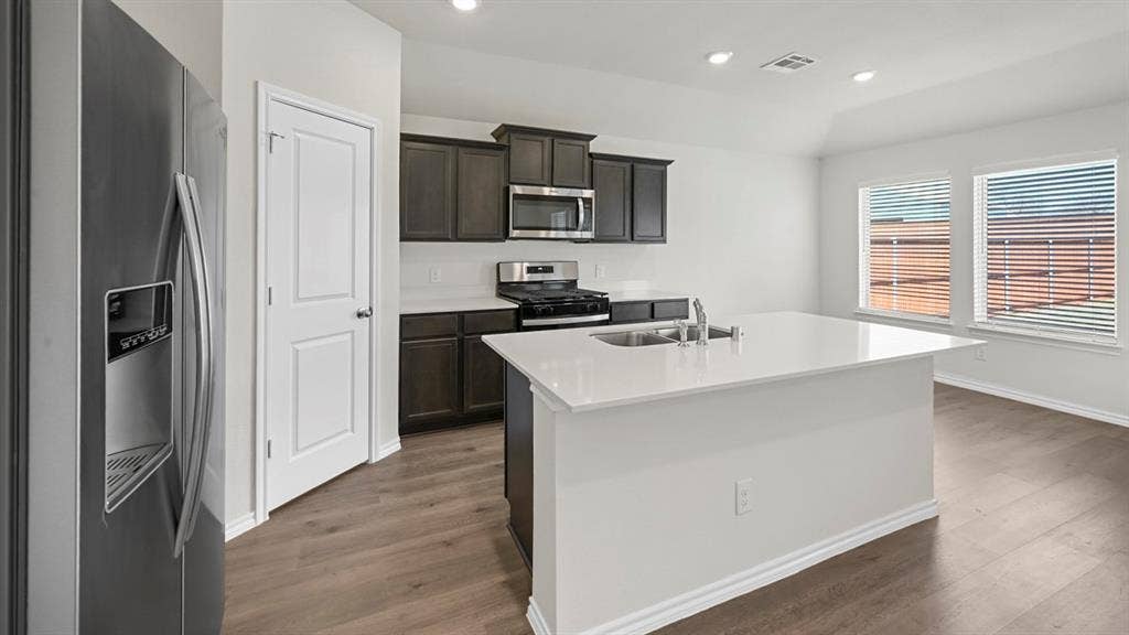 Kitchen featuring stainless steel appliances, a kitchen island with sink, recessed lighting, dark wood-style floors, and light stone countertops