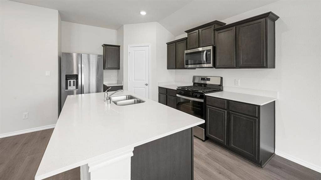 Kitchen with stainless steel appliances, light wood-style flooring, a kitchen island with sink, light stone counters, and vaulted ceiling