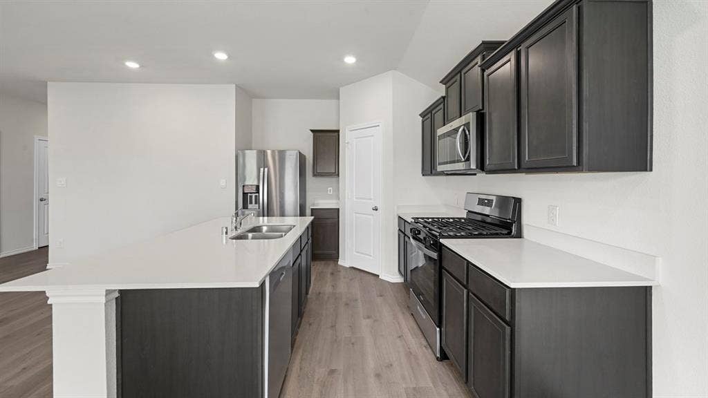 Kitchen featuring stainless steel appliances, an island with sink, light wood-type flooring, recessed lighting, and light stone countertops