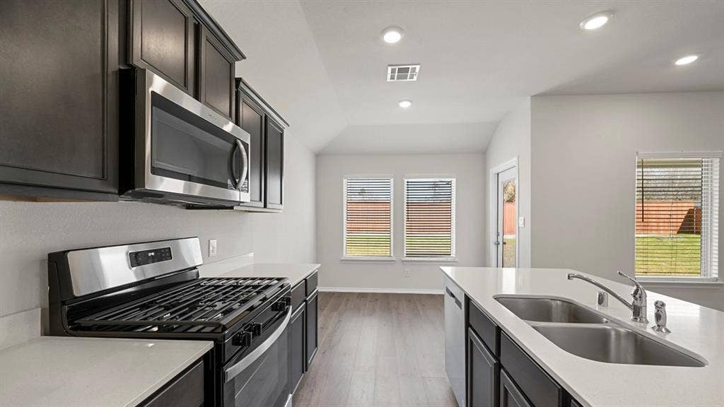 Kitchen with stainless steel appliances, dark cabinetry, light wood-style floors, recessed lighting, and light stone counters