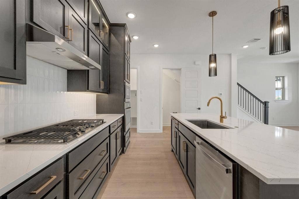 2852 Yampa Drive, McKinney, TX 75071 Modern kitchen featuring a gas cooktop, stainless steel hood, quartz countertops, a large island with an undermount sink, and dark cabinetry with brass hardware