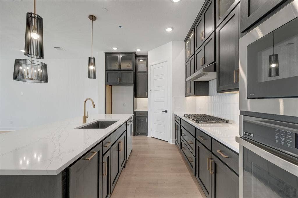 2852 Yampa Drive, McKinney, TX 75071 Gourmet kitchen featuring an oversized island with an undermount sink and gold-finish faucet, dark cabinetry, and light wood-finish flooring