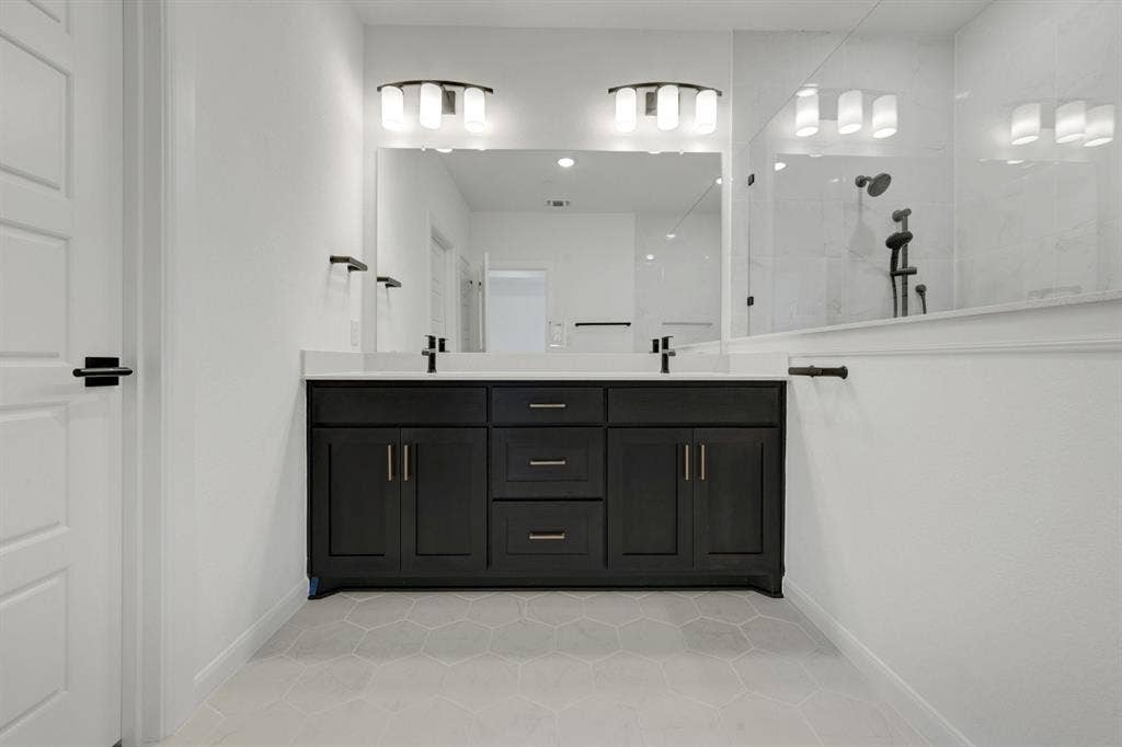2852 Yampa Drive, McKinney, TX 75071 Dual vanity with black cabinetry, white countertops, hexagon tile flooring, and a glass-enclosed shower with black fixtures