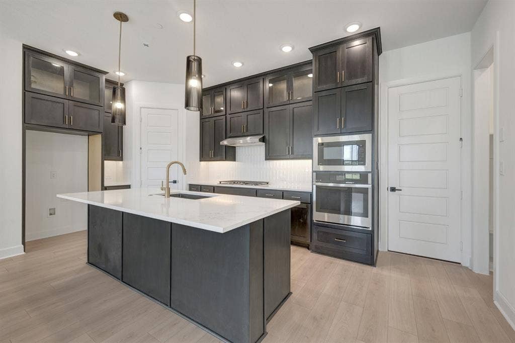 2852 Yampa Drive, McKinney, TX 75071 Kitchen featuring a spacious island with a white countertop, dark cabinetry, stainless steel appliances, and wood-finish flooring