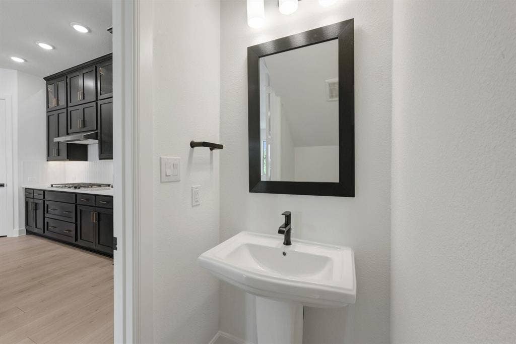 2852 Yampa Drive, McKinney, TX 75071 Pedestal sink with matte black faucet, framed mirror, and contemporary light fixture