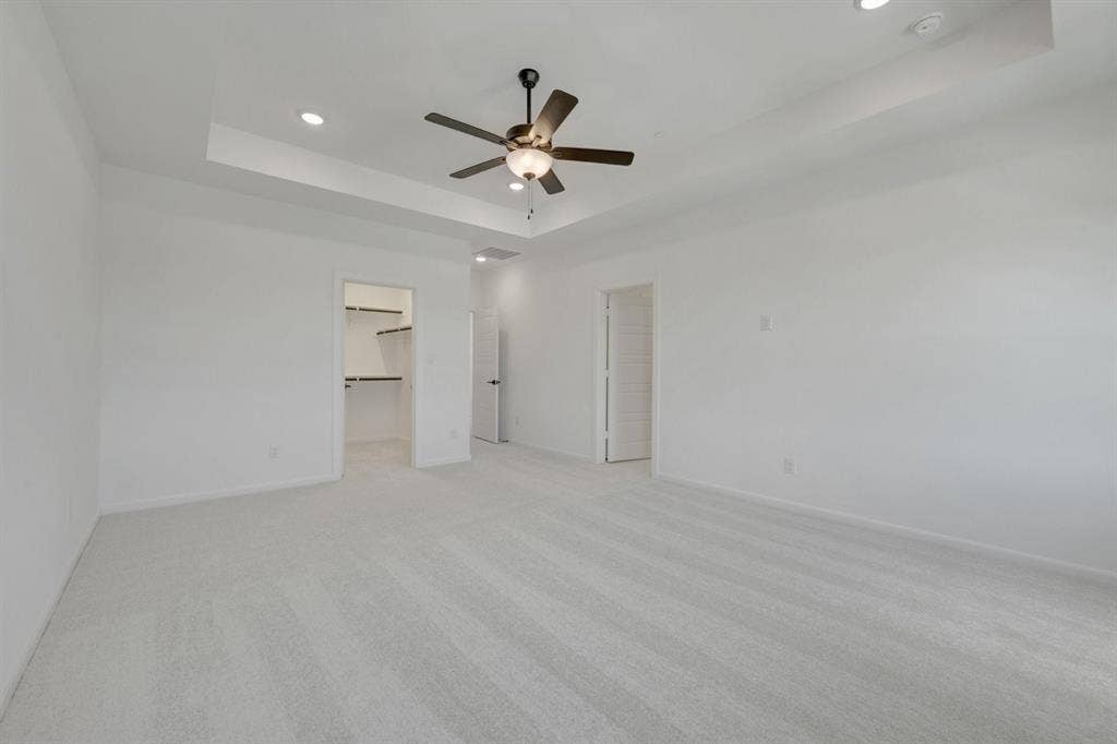 2852 Yampa Drive, McKinney, TX 75071 Spacious room featuring light-toned carpet, a tray ceiling with recessed lighting, and a dark-finished ceiling fan