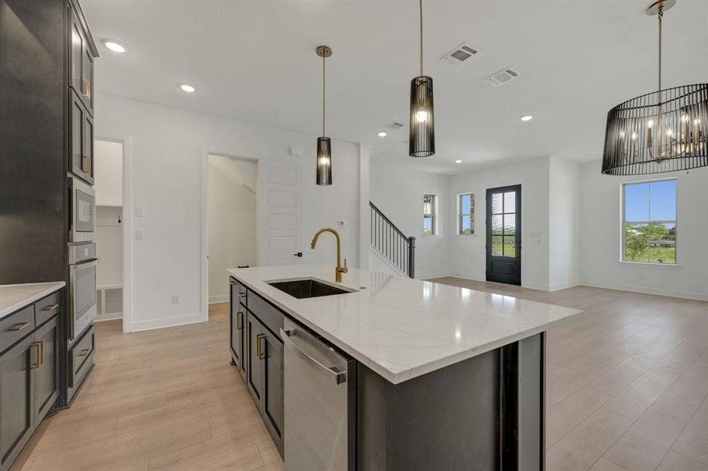 2852 Yampa Drive, McKinney, TX 75071 Contemporary kitchen featuring a large island with white stone countertop, integrated sink, and bronze-finish faucet