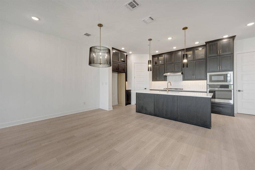 2852 Yampa Drive, McKinney, TX 75071 Modern kitchen featuring an island with a white countertop, dark cabinetry, and integrated stainless steel appliances