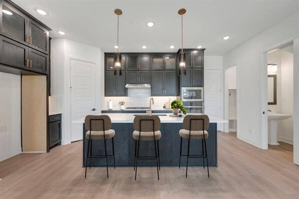 2852 Yampa Drive, McKinney, TX 75071 Modern kitchen featuring a central island with seating, dark shaker cabinetry, stainless steel appliances, and wood-finish flooring