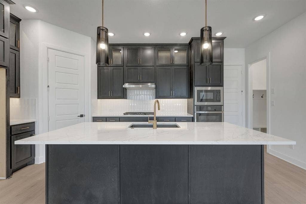 2852 Yampa Drive, McKinney, TX 75071 Kitchen featuring dark cabinetry, a large center island with a white stone countertop, a gold-finish faucet, and stainless steel appliances