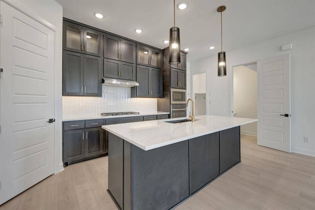 2852 Yampa Drive, McKinney, TX 75071 Modern kitchen featuring dark cabinetry, white quartz countertops, stainless steel appliances, and light wood-finish flooring