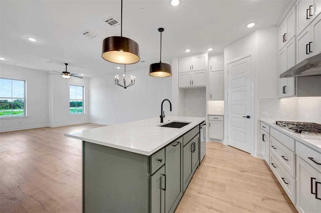 2860 Yampa Drive, McKinney, TX 75071 Open-concept kitchen featuring an island with a built-in sink, white countertops, a gas range with an overhead vent, and wood-finish flooring throughout