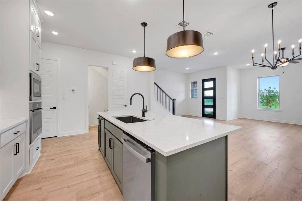 2860 Yampa Drive, McKinney, TX 75071 Open-concept kitchen featuring a spacious island with a countertop and built-in sink, stainless steel appliances, white cabinetry, and wood-finish flooring