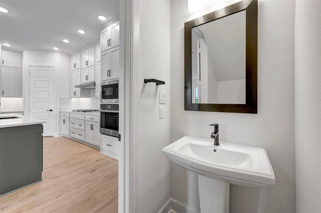 2860 Yampa Drive, McKinney, TX 75071 Pedestal sink with a dark framed mirror and wall-mounted light fixture