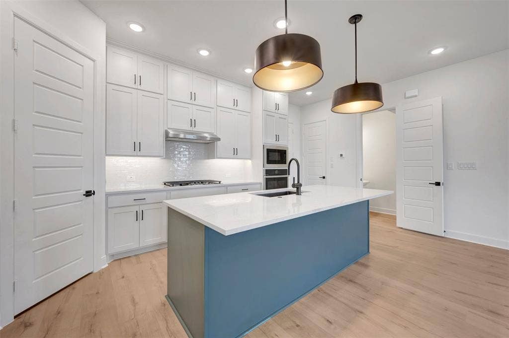 2860 Yampa Drive, McKinney, TX 75071 Contemporary kitchen featuring a blue-toned island with a white countertop and dark pendant lighting