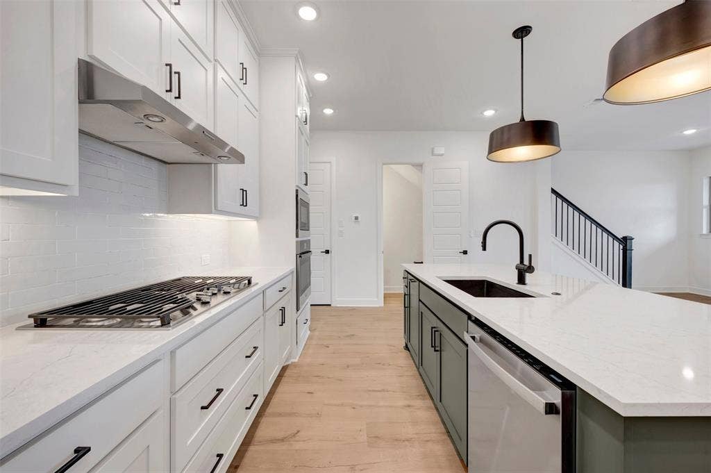 2860 Yampa Drive, McKinney, TX 75071 Contemporary kitchen featuring a gas range, stainless steel appliances, white cabinetry with dark hardware, a center island with a sink, and wood-finish flooring
