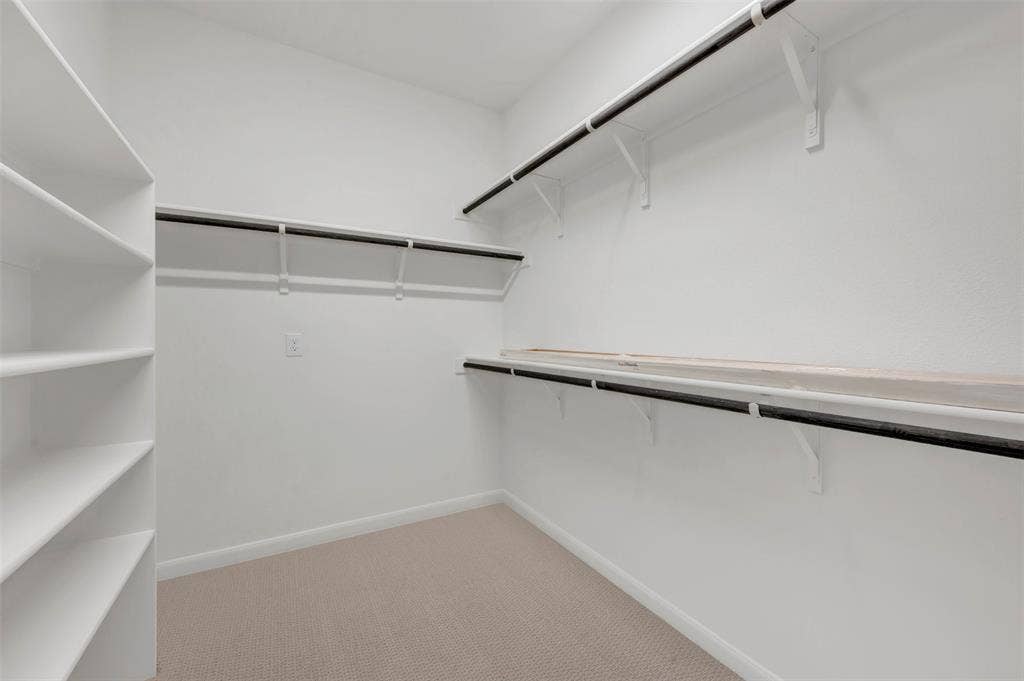 2860 Yampa Drive, McKinney, TX 75071 Walk-in closet featuring built-in shelving, multiple hanging rods, overhead storage shelves, and neutral carpeting