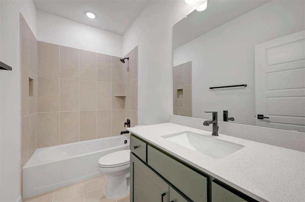 2860 Yampa Drive, McKinney, TX 75071 Bathroom featuring a built-in tub with tile surround, a single vanity with a quartz countertop, an integrated sink, and matte black fixtures