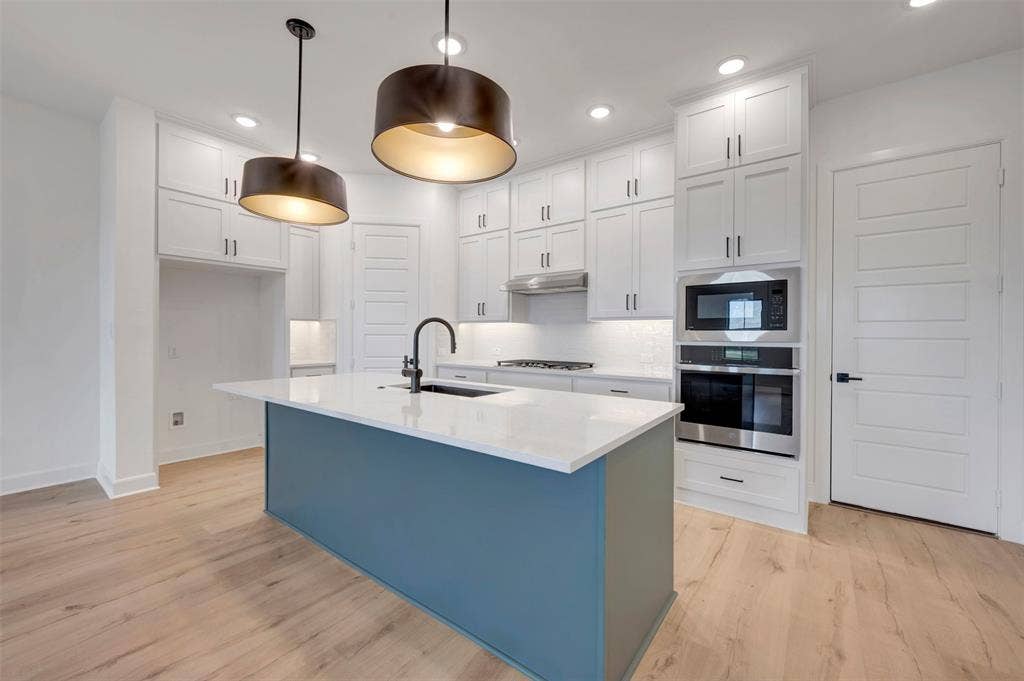 2860 Yampa Drive, McKinney, TX 75071 Contemporary kitchen featuring a prominent island with a white countertop and dark blue base, complemented by two large pendant lights