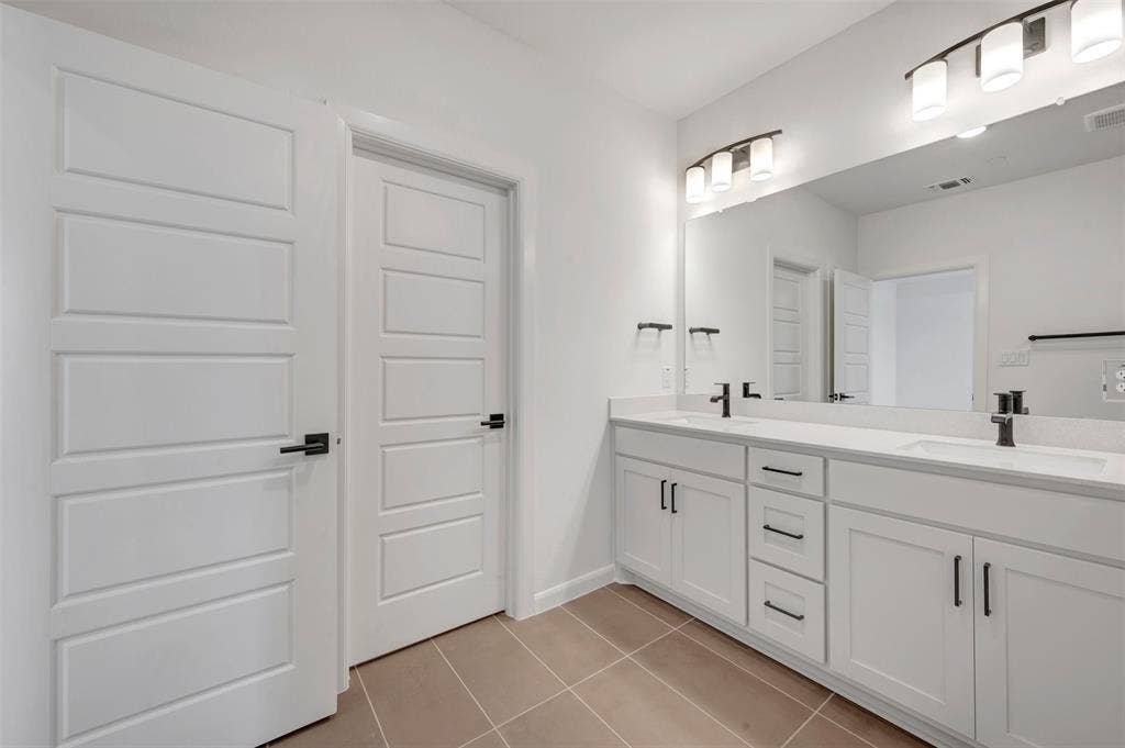 2860 Yampa Drive, McKinney, TX 75071 Double vanity featuring white cabinetry, integrated sinks, black hardware, and an expansive wall mirror