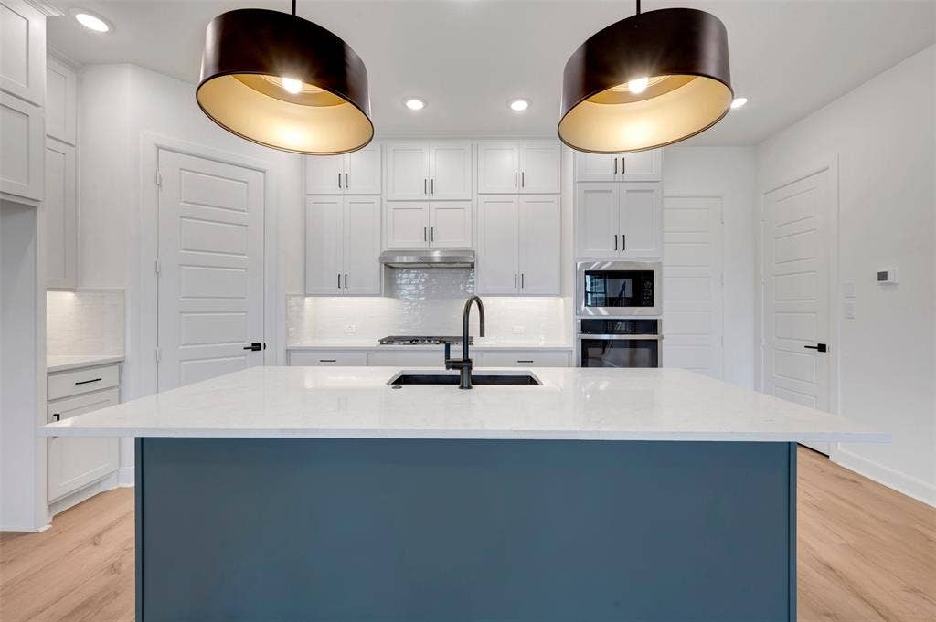 2860 Yampa Drive, McKinney, TX 75071 Kitchen featuring a large island with a white countertop and blue-finish base, dual contemporary pendant lighting, white shaker cabinetry, stainless steel appliances, and wood-finish flooring