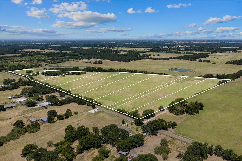 Expansive undeveloped land featuring multiple subdivided parcels, surrounding wooded areas, and distant agricultural fields