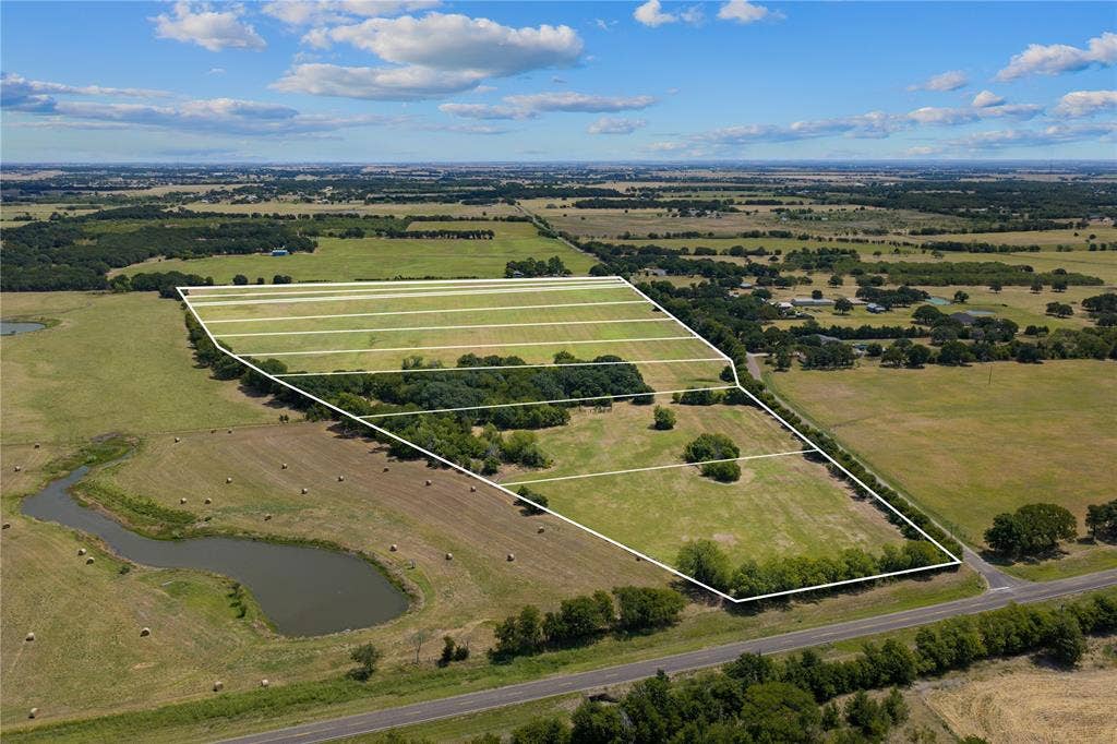Expansive property featuring a pond, mature trees, open fields, and road frontage