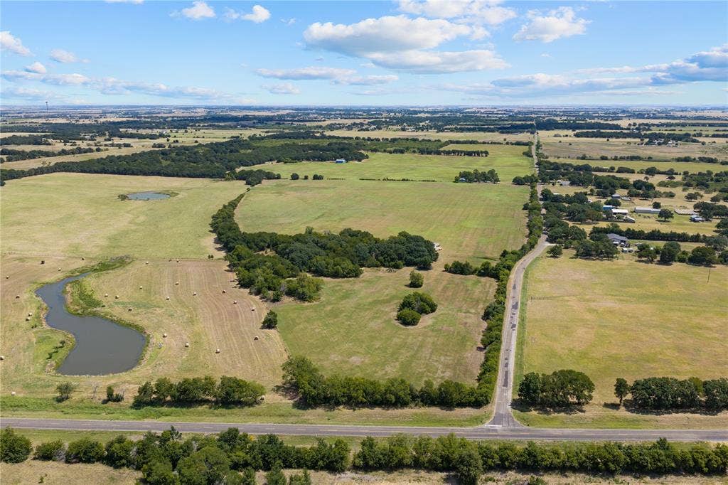 Expansive land parcel featuring a winding roadway, established trees, and two distinct water features