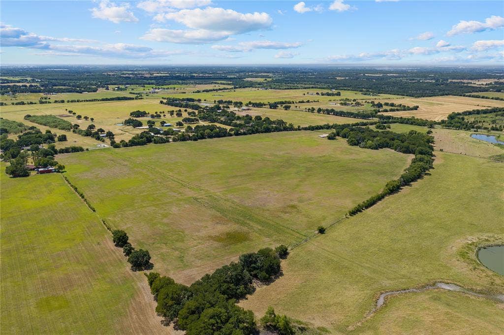 Expansive acreage featuring open fields, scattered mature trees, and a natural pond