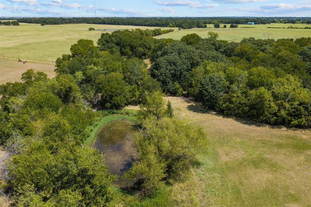 Expansive landscape featuring wooded areas, open fields, and a natural pond