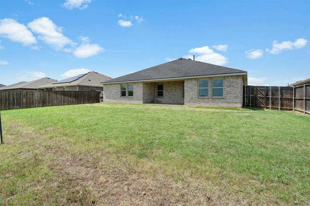 653 Bunker Hill Road, Fate, TX 75189 Expansive backyard featuring a manicured lawn, full privacy fencing, brick exterior, dark shingle roofing, and multiple rear-facing windows