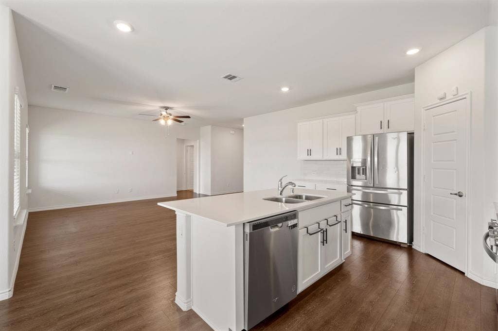 653 Bunker Hill Road, Fate, TX 75189 Open-concept living space featuring a central kitchen island with a double basin sink, white cabinetry with dark hardware, stainless steel appliances, and wood-finish flooring