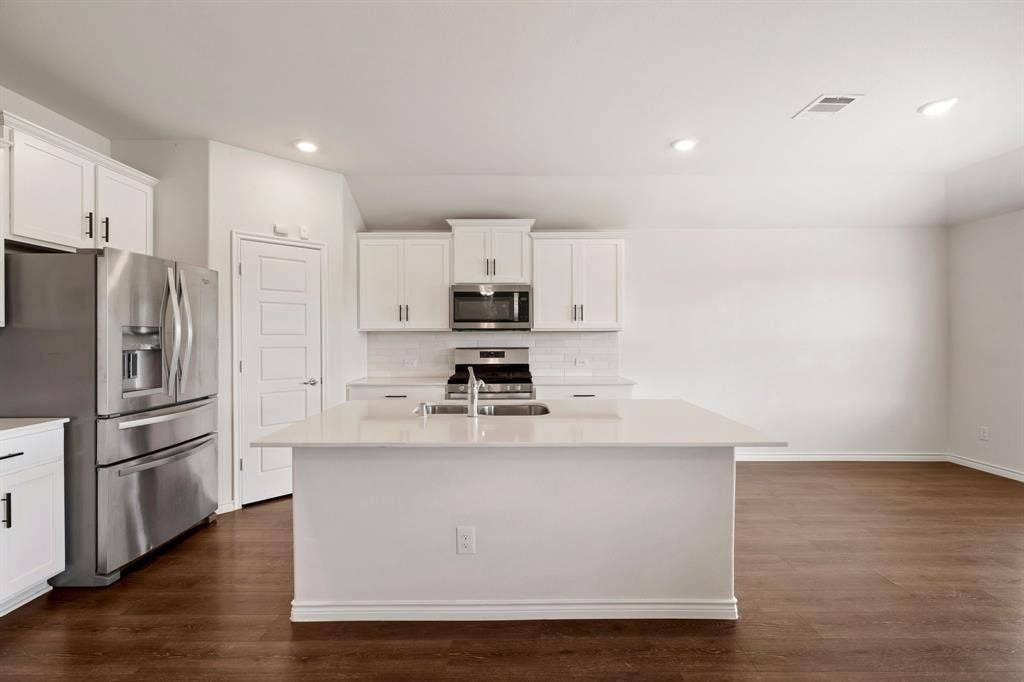 653 Bunker Hill Road, Fate, TX 75189 Kitchen featuring a central island with an undermount sink, white cabinetry with dark hardware, stainless steel appliances, and wood-finish flooring