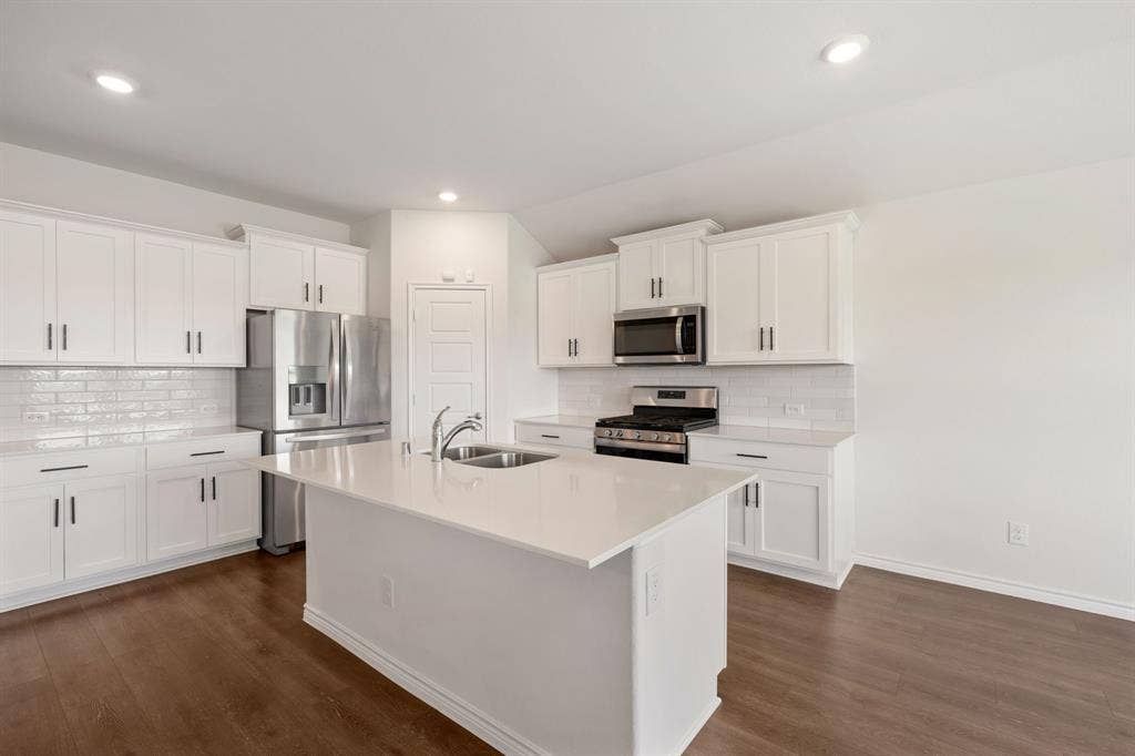 653 Bunker Hill Road, Fate, TX 75189 Open-concept kitchen featuring an island with an undermount sink, white cabinetry, a subway tile backsplash, stainless steel appliances, and wood-finish flooring