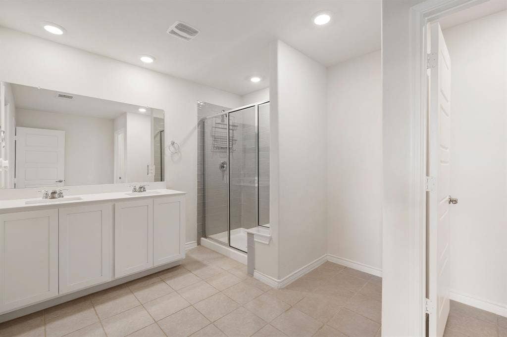 653 Bunker Hill Road, Fate, TX 75189 Bathroom featuring a dual vanity with white cabinetry, a large frameless mirror, and a glass-enclosed shower with subway tile surround