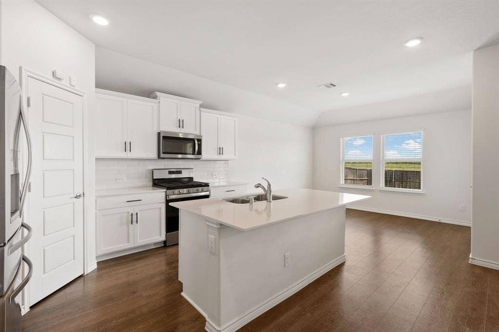 653 Bunker Hill Road, Fate, TX 75189 Modern kitchen featuring an island with a stainless steel sink, white cabinetry with dark hardware, stainless steel appliances, and a white subway tile backsplash