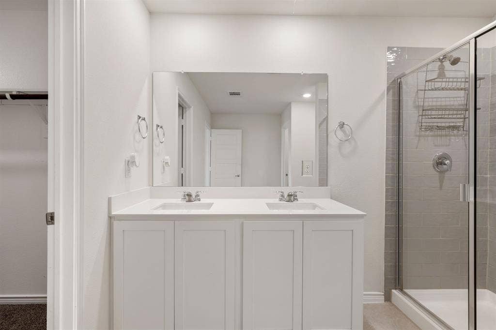 653 Bunker Hill Road, Fate, TX 75189 Bathroom featuring a dual vanity with white cabinetry and integrated sinks, a large wall-mounted mirror, and a glass-enclosed shower with subway tile surround