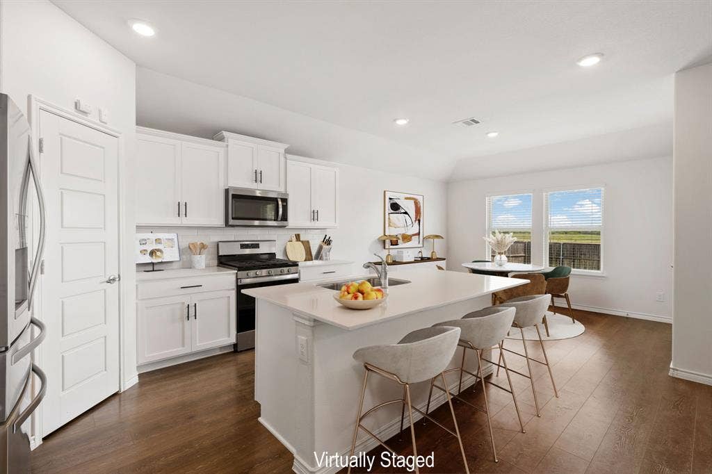 653 Bunker Hill Road, Fate, TX 75189 Kitchen featuring a large central island with seating, white shaker-style cabinetry, stainless steel appliances, wood-finish flooring, and recessed lighting