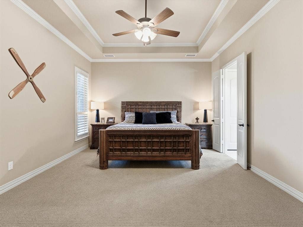 2115 N Hill Drive, Irving, TX 75038 Primary bedroom with light colored carpet, ornamental molding, a raised ceiling, multiple windows with custom wood plantation shutters and solid 8 foot wood doors.