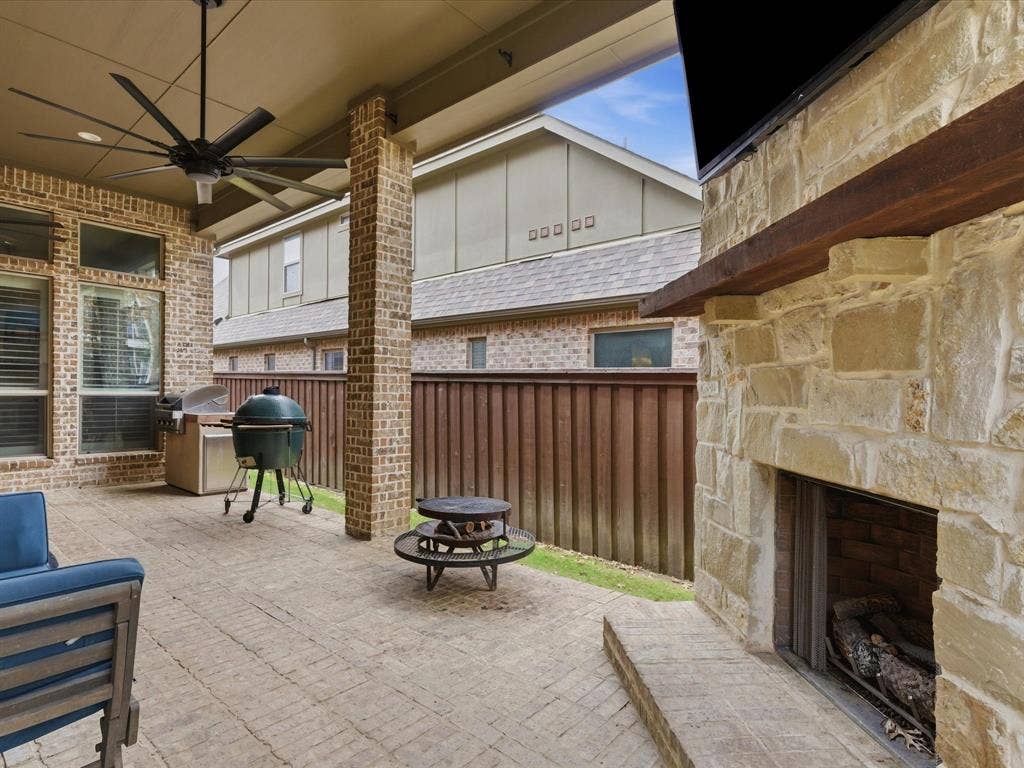 2115 N Hill Drive, Irving, TX 75038 View of patio / terrace with ceiling fan, a grill, an outdoor stone fireplace and board on board cedar wood fence.