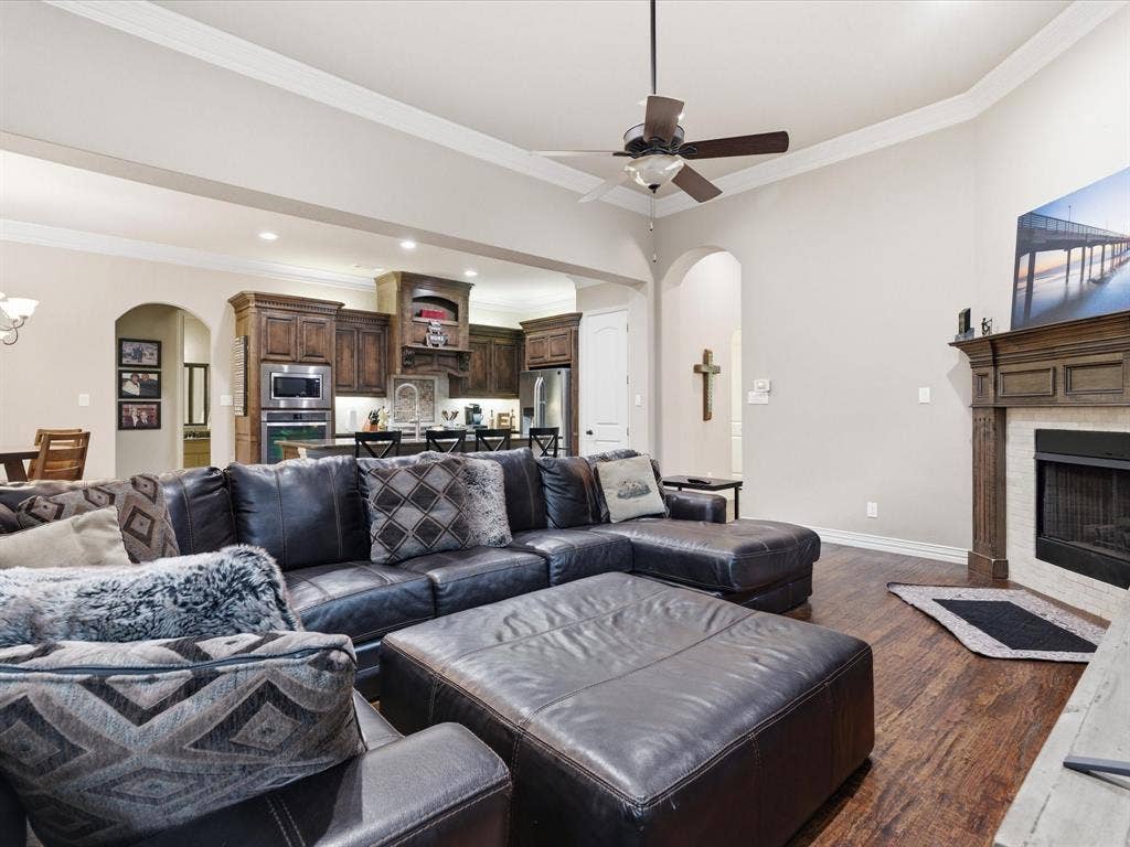 2115 N Hill Drive, Irving, TX 75038 Living room with arched walkways, a fireplace, dark wood-type flooring, crown molding, and a ceiling fan