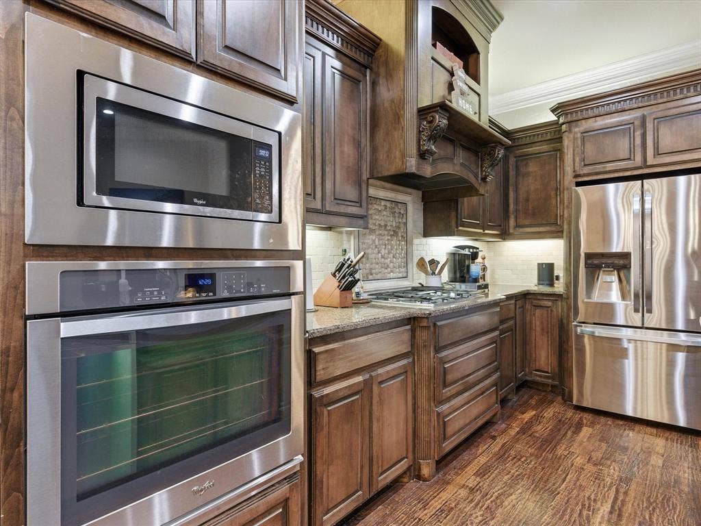 2115 N Hill Drive, Irving, TX 75038 Kitchen featuring stainless steel appliances, hand scraped oak floors, granite countertops, crown molding, under counter lighting, and decorator backsplash.
