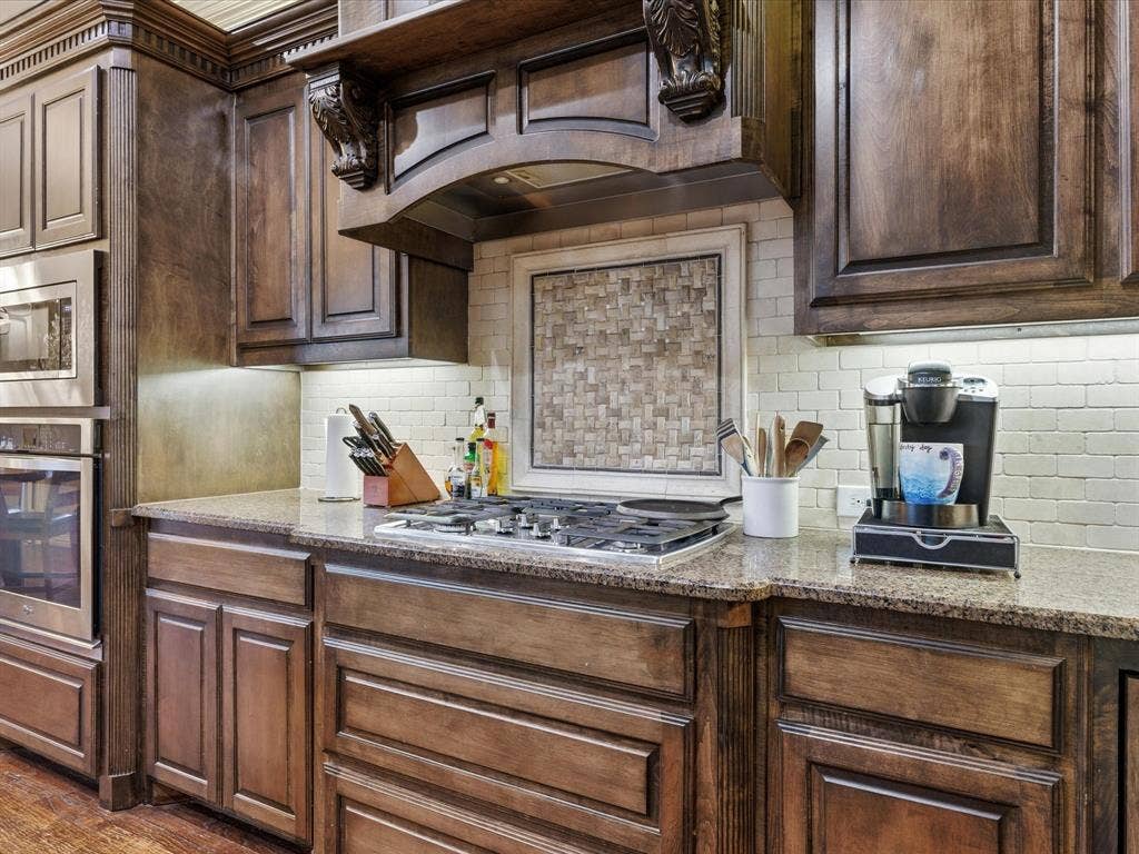 2115 N Hill Drive, Irving, TX 75038 Kitchen featuring dark wood finish cabinets, stainless steel appliances including 4 burner gas stove, undercounted lighting, granite counters, and custom backsplash
