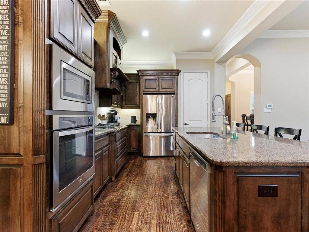 2115 N Hill Drive, Irving, TX 75038 Kitchen featuring a huge breakfast bar area, dark wood finish cabinetry, stainless steel appliances including 4 burner gas stove, walk-in pantry, granite counters, and crown molding
