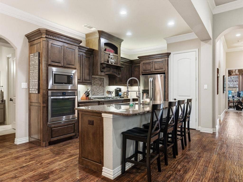 2115 N Hill Drive, Irving, TX 75038 Kitchen featuring arched walkways, dark wood finish cabinetry, stainless steel appliances, hand scraped wood finished floors, and crown molding.