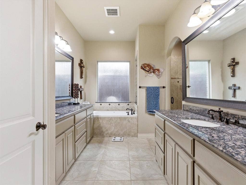 2115 N Hill Drive, Irving, TX 75038 Primary bathroom with two vanities, a garden tub, and a walk in shower with bench.