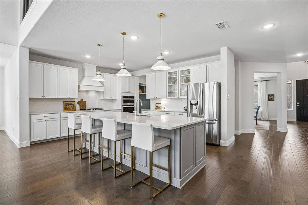 13674 Carmenita Drive, Frisco, TX 75035 Two tone kitchen with a spacious island, stainless steel appliances, glass insert cabinets, a breakfast bar, and dark wood-type flooring