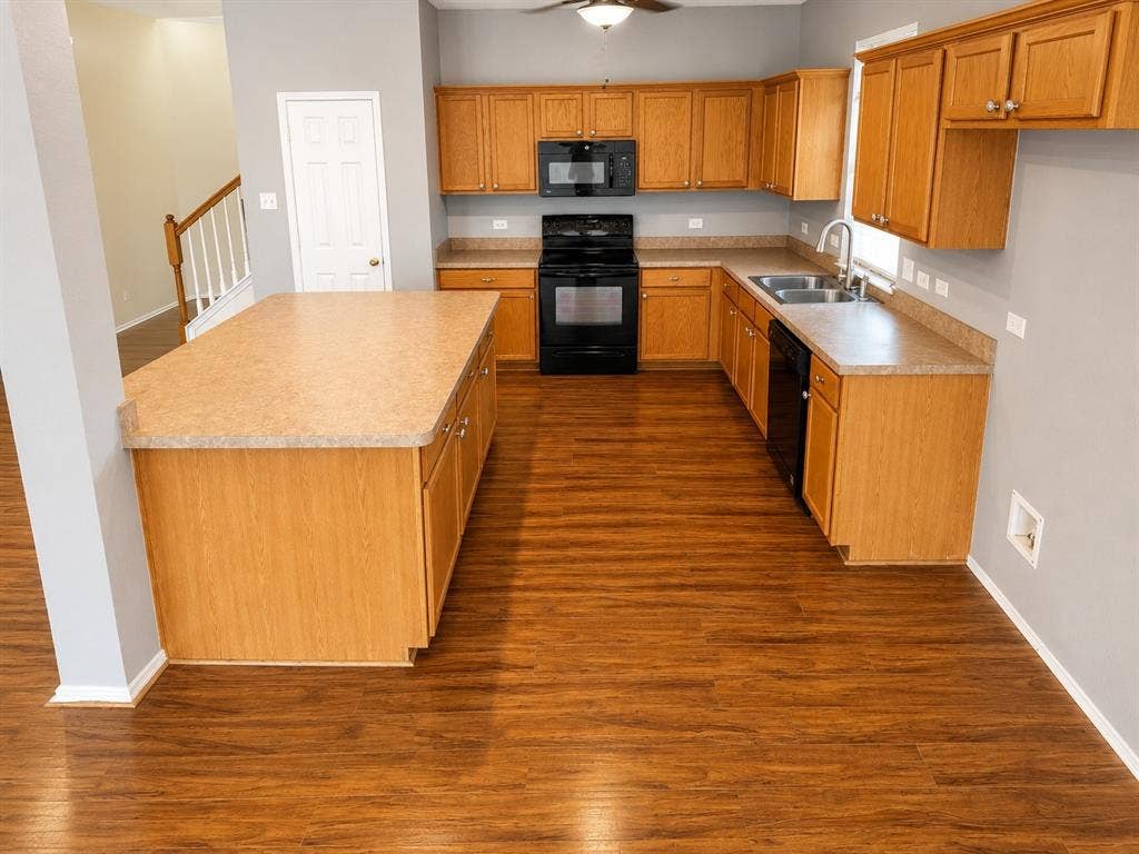103 Denali Court, Terrell, TX 75160 Kitchen featuring wood-finish flooring, a central island with countertop, coordinating wood cabinetry, black appliances including a range and microwave, and a double-basin sink with a gooseneck faucet